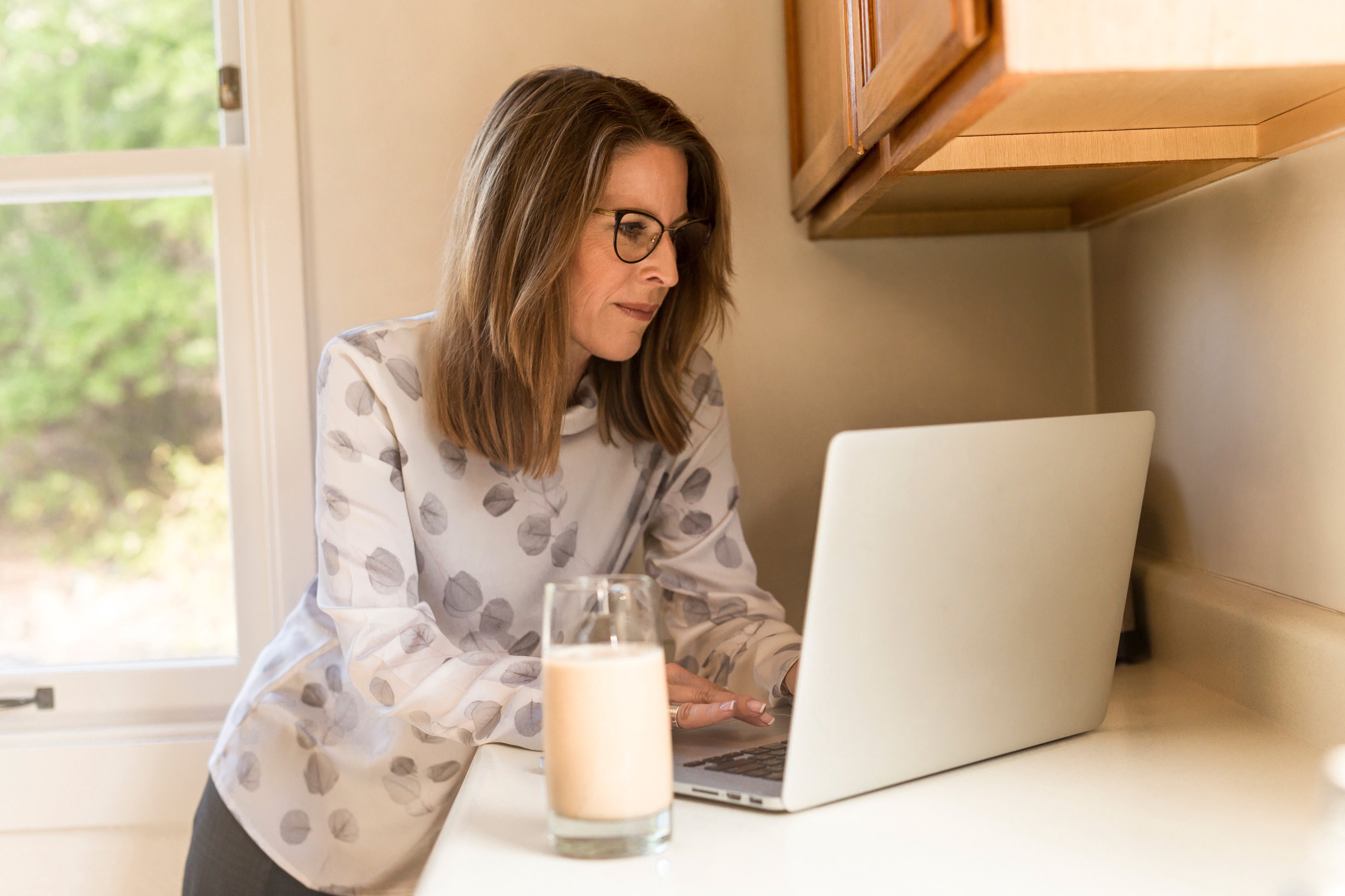 person in kitchen on laptop drinking a glass of milk