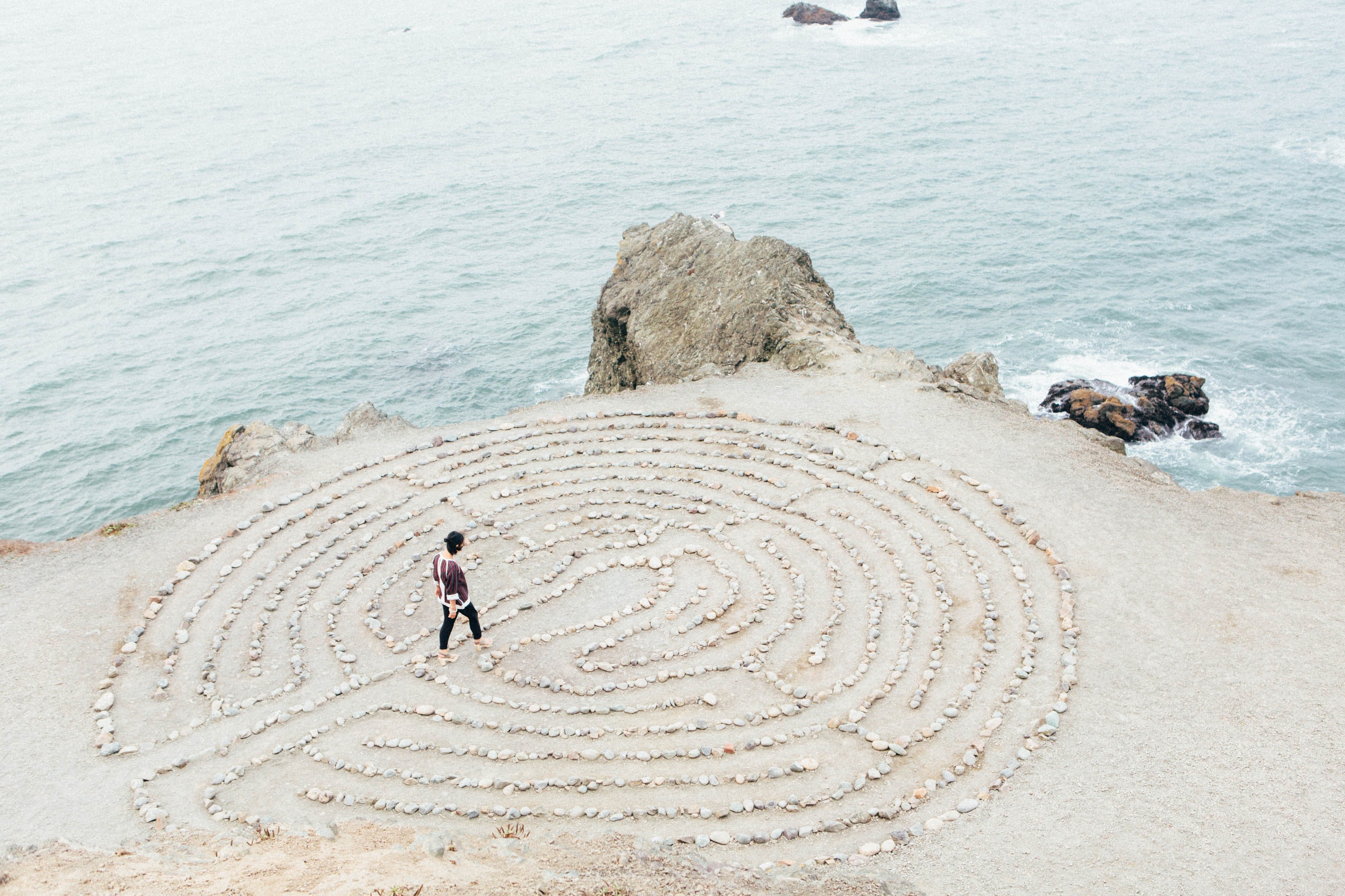 person walking through a maze made of pebbles on beach